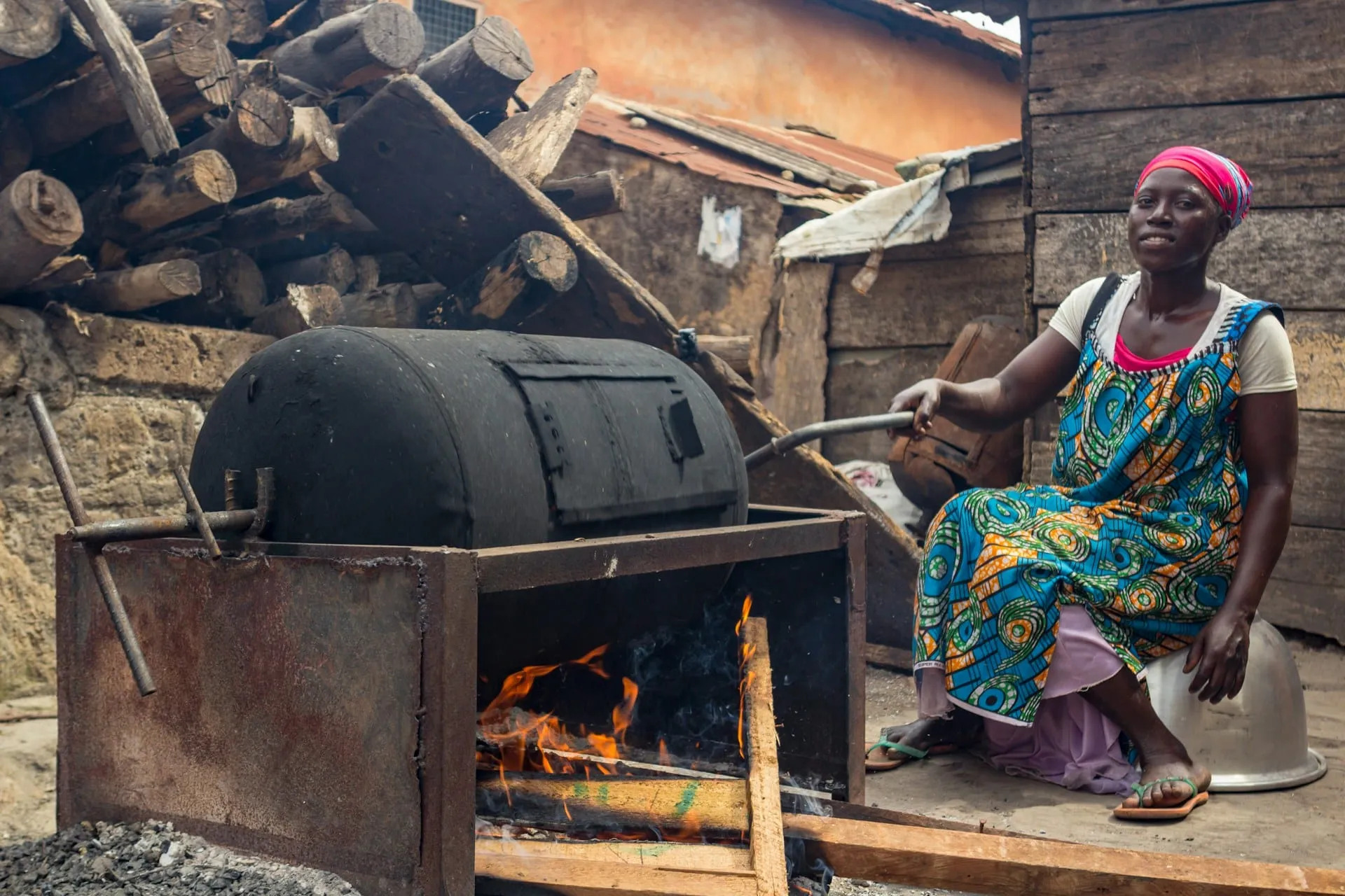 A woman tending a wood-fired metal drum stove