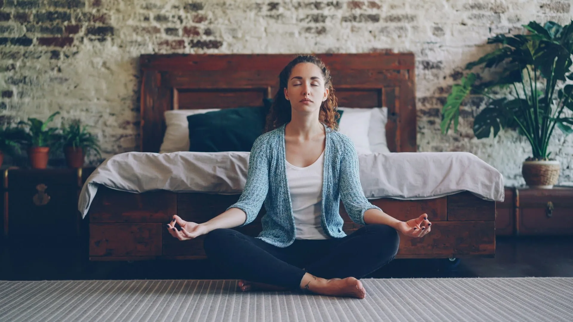 A woman meditating cross-legged in a bedroom