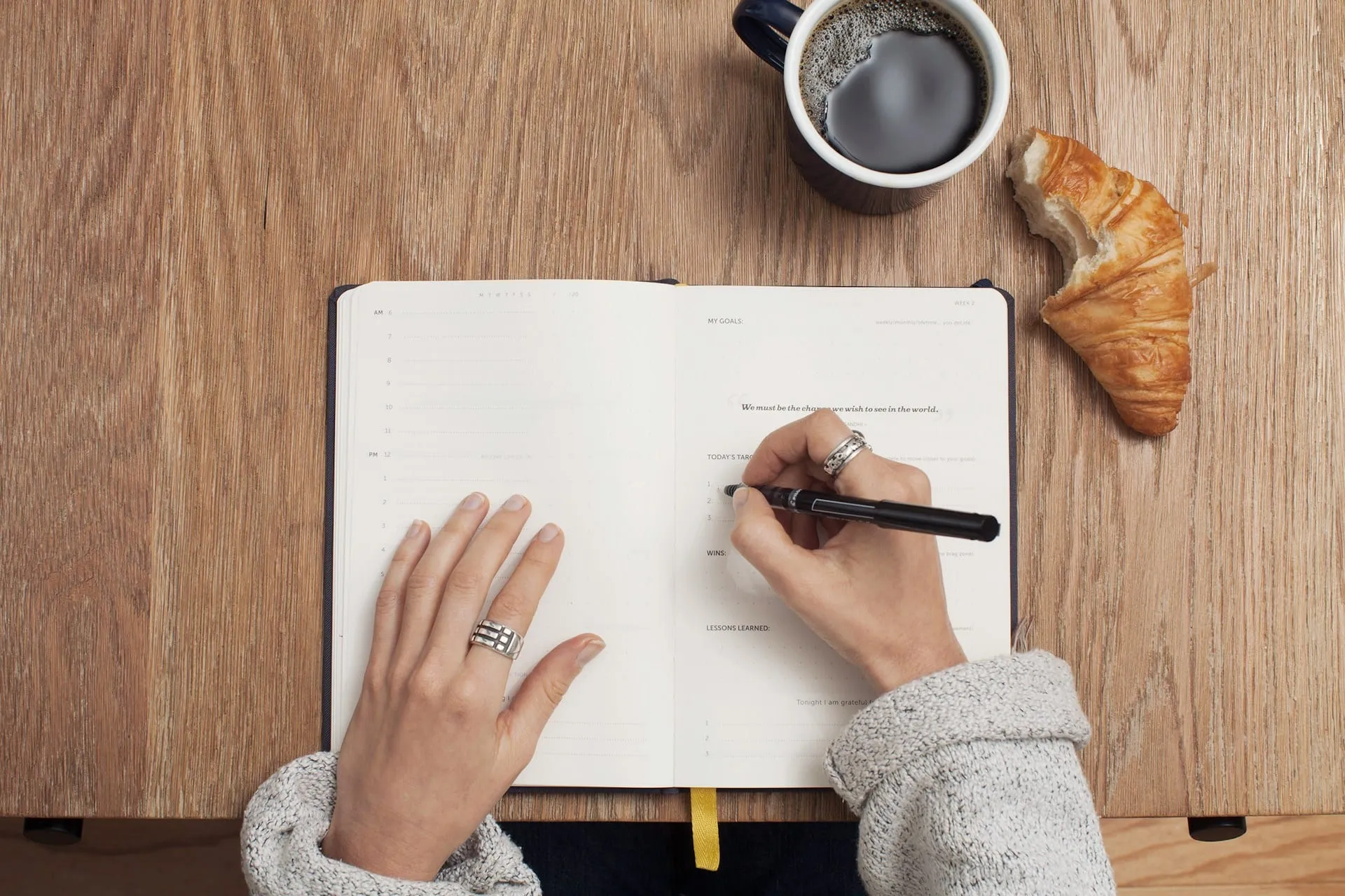 Hands writing in a journal beside a cup of coffee